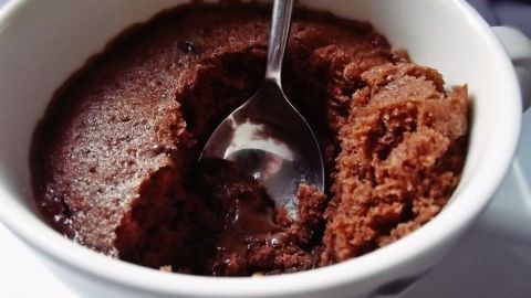 Eine Tasse mit Schokoladenkuchen wird mit einem Löffel umgerührt, in einem gemütlichen Küchenumfeld.