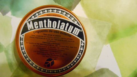 Eine runde Dose mit der Aufschrift "Mentholatum" liegt auf einem farbenfrohen Hintergrund und könnte bei Hustenattacken helfen.