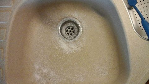 Eine Steinspüle ist beige und hat Rückstände, während sie sich im Reinigungsprozess in einer Küche befindet.