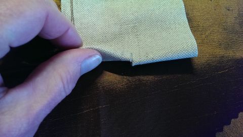 Eine Hand hält einen schmalen Stoff, während sie ihn vorsichtig aufschneidet, auf einem braunen Untergrund.
