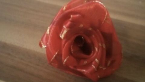 Eine rote Rose aus Geschenkband liegt auf einer Holzoberfläche, dekorativ und kunstvoll gestaltet, wirkt elegant.