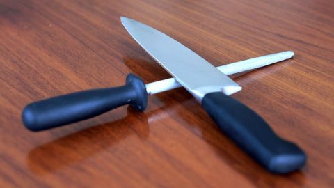 Auf einem Holztisch liegen ein scharfes Küchenmesser und ein Schleifstab, bereit für die Messerschärfung.