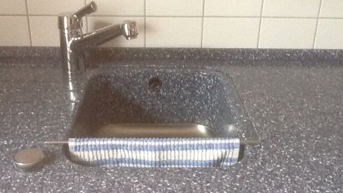 Ein Spültuch liegt auf einer glänzenden Küchentheke vor einem modernen Wasserhahn, bereit zur Verwendung.