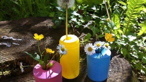 Bunte Vasen in pink, gelb und blau stehen im Grünen und halten frische Blumen, die die Umgebung aufhellen.