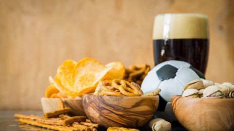 Knusprige Snacks und ein Glas Bier liegen auf einem Tisch, während ein Fußball die EM-Party-Stimmung einfängt.