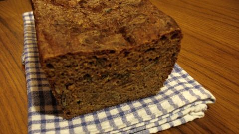 Ein rustikales Dinkel-Karotten-Brot liegt auf einem karierten Geschirrtuch, umgeben von einer Holzoberfläche.