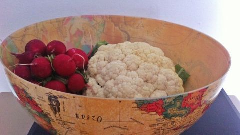 Ein alter Globus dient als Schale und ist mit Radieschen und Blumenkohl gefüllt, auf einem schwarzen Untergrund.