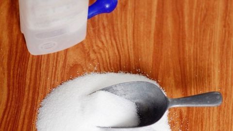 Ein Behälter mit Kochsalzlösung steht neben einem Haufen Salz, während ein Messlöffel darin steckt.
