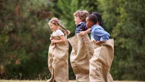 Kindern in großen Säcken hüpfen fröhlich über eine Wiese, ideal für einen stressfreien Kindergeburtstag im Freien.