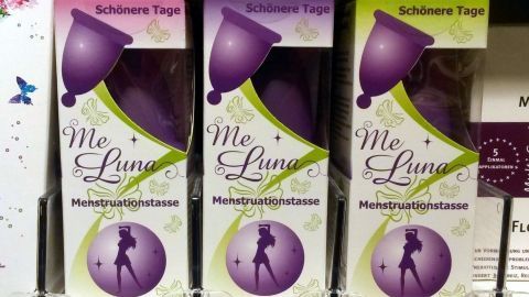 Drei Verpackungen für Menstruationskappen stehen nebeneinander im Regal, jede mit einem stilisierten weiblichen Silhouetten-Design.