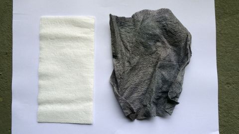In der Handtasche habe ich immer ein Anti-Verfärbetuch griffbereit, um Schmutzspritzer von meinen Schuhen wegzuwischen. Zwei Tücher liegen nebeneinander auf einem weißen Hintergrund, eines weiß und sauber, das andere grau und gebrauchsfertig.