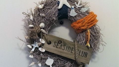 Ein maritimer Türkranz hängt an einer Wand, geschmückt mit Muscheln, einem Seestern und dem Schild "SEASIDE CLUB".