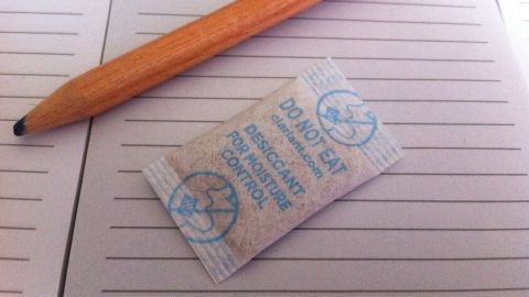 Ein Silica-Gel-Beutel liegt auf einem Notizblock, während ein Bleistift daneben für Notizen bereitliegt.