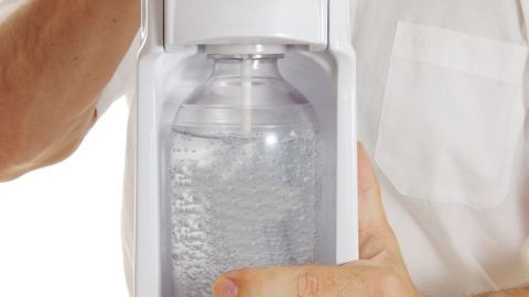 Eine Person hält einen SodaStream, während sie eine sprudelnde Flasche vorbereitet, um Wasser zu karbonisieren.