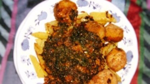 Ein Teller mit Curry aus Karottengrün, Hühnerfleischbällchen und Kartoffelwedges auf einem bunten, gestreiften Tuch.