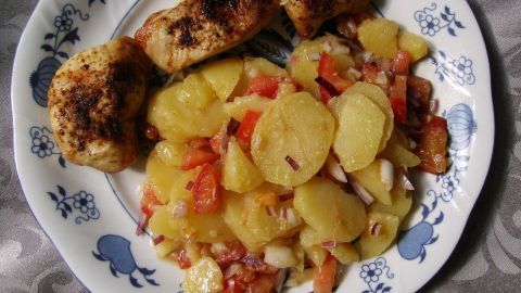 Eine Telleransicht zeigt Kartoffelsalat mit Tomaten und Hähnchenmedaillons, garniert mit frischem Gemüse und Kräutern.