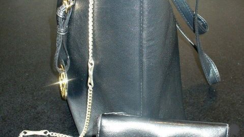 Ein schwarzes Portemonnaie ist an einer Kette befestigt, die am Innenrand einer Handtasche hängt.