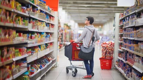 Eine Person steht mit einem Einkaufswagen in einem Supermarkt und schaut auf die Regale voller Produkte, um Gratis Produkte zu finden.
