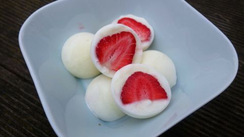 Auf einem hellblauen Teller liegen geformte Joghurtkugeln mit geviertelten, frischen Erdbeeren in der Mitte.