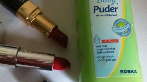 Ein Fläschchen Baby-Puder steht neben roten Lippenstiften auf einem weißen Untergrund, bereit für clevere Anwendungen.
