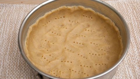 Ein ungebackener Kuchenteig liegt in einer runden Springform auf einem hellen Untergrund, bereit zum Backen.