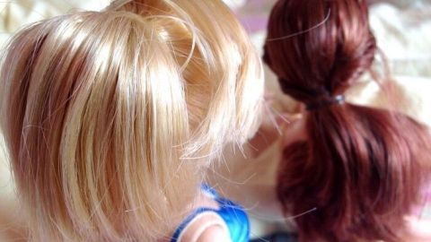 Verfilzte Barbie Haare werden von zwei Puppen mit unterschiedlichen Frisuren in einer entspannten Umgebung betrachtet.