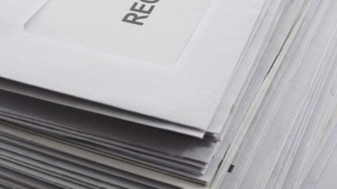 Eine Stapel von Briefen, die auf einem Tisch liegen, zeigt nur die Aufschrift „RECHNUNG“ auf den Umschlägen.