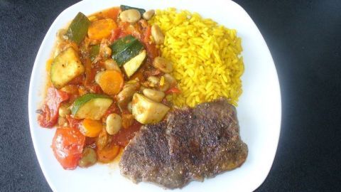 Ein Teller zeigt Gemüsereis mit buntem Gemüse, dazu ein Stück Steak in einem schlichten, modernen Ambiente.