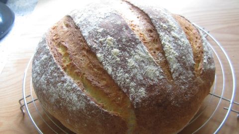 Ein frisch gebackenes Kartoffelbrot liegt auf einem Rost, umgeben von einer hellen Küchenoberfläche.