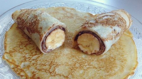 Zwei gefüllte Pfannkuchen rollen auf einem Teller, jeder mit einer Banane gefüllt, in einem hellen, dekorativen Umfeld.