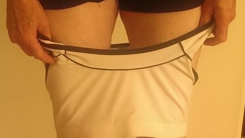 Ein Sport-BH wird entspannt über die Beine angezogen, während die Person in kurzen Hosen in einem hellen Raum steht.