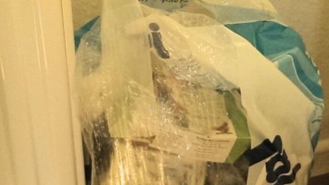 Eine durchsichtige Tüte mit Toilettenpapierverpackungen steht neben einem Heizkörper in einem Badezimmer.