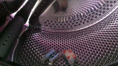 Eine glänzende Waschmaschine zeigt die Trommel von innen, während zwei farbige Gegenstände darin liegen und sie sauber wirkt.