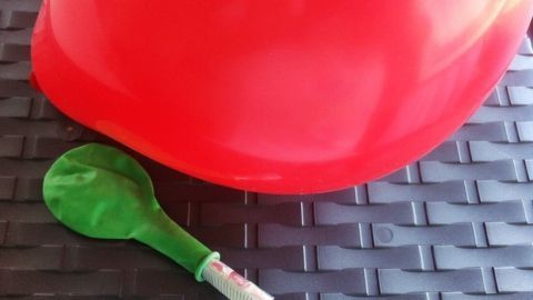 Rote Luftballons liegen auf einer dunklen Oberfläche, während ein grüner Ballon mit Geldgeschenk vorbereitet wird.