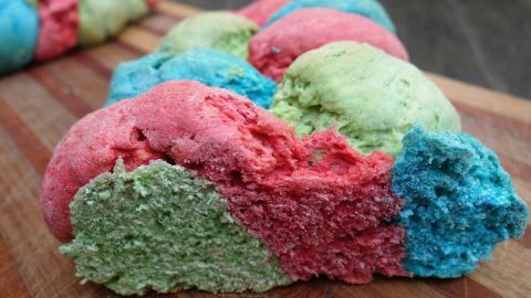 Bunter Hefezopf in leuchtenden Farben liegt auf einem Holzbrett und lädt zum Genießen ein. Aromatisch und frisch.