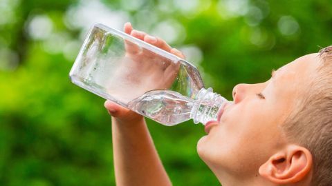 Ein Junge trinkt aus einer Wasserflasche, um sich in einer grünen Umgebung mit frischem Wasser zu hydrieren.