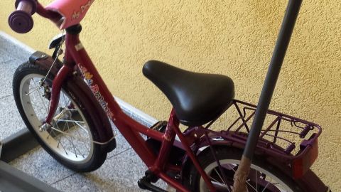 Ein rotes Kinderfahrrad steht auf einem Kiesboden, während jemand versucht, es mit einem Gestell zu stabilisieren.