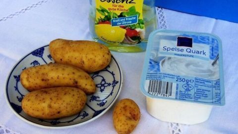 Auf einem Teller liegen mehrere Kartoffeln, während eine Flasche Zitronenaroma und ein Becher Dip daneben stehen.