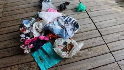Ein Haufen bunter Plastiktüten liegt chaotisch auf einem Holzboden, umgeben von natürlichem Licht im Außenbereich.
