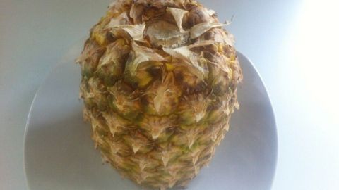 Eine ganze Ananas liegt auf einem weißen Teller, bereit zur Aufbewahrung in einer hellen Küchenumgebung.