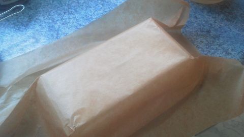 Ein Stück Backpapier liegt in einer Backform, bereit zum Backen, um das Einfetten zu vermeiden. Der Hintergrund zeigt eine blaue Arbeitsplatte.