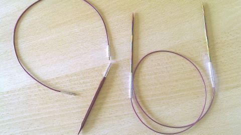 Zwei Stricknadeln liegen auf einem hellen Tisch, bereit zum Stricken, um die Stärken der KnitPro Symfonie und Cubics zu vergleichen.