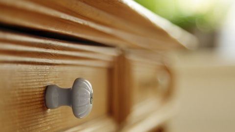 Eine Holzschublade mit einem grauen Knopf steht im Fokus, während das Licht freundlich auf die Pflegeoberfläche fällt.
