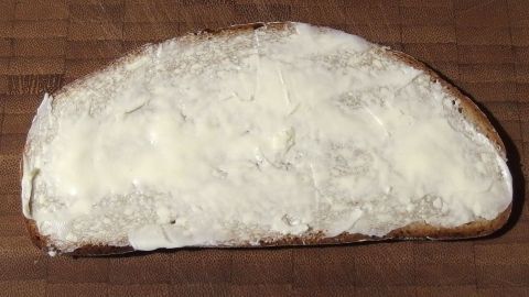 Ein Stück Brot liegt auf einem Holzbrett, gleichmäßig mit harter Butter bestrichen, bereit zum Verzehr.
