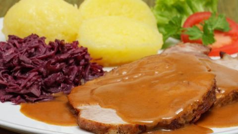 Ein Teller mit saftigem Fleisch, überzogen mit Fertigsoße, dazu Kartoffeln, Rotkohl und frischer Salat.