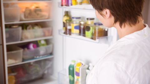 Ein Kühlschrank steht offen, während eine Person nach der Ursache für Wasser im Kühlschrank sucht, um ihn zu „trockenlegen“.