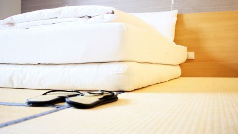 Ein Futon liegt gestapelt auf einem Tatami-Boden, während ein Paar Sandalen daneben steht, in einem modernen Raum.