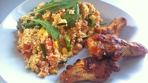 Ein bunter Couscous-Salat mit Rucola und knusprigen Hähnchenstücken auf einem weißen Teller, appetitlich angerichtet.