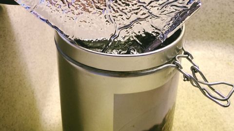 Ein Kaffeepulverbehälter wird unter einem ausgeklappten, reflektierenden Deckel in einer Spüle platziert, um Spuren zu vermeiden.