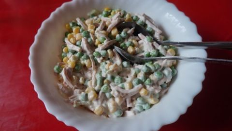 Ein bunter Salat aus Gemüse und Hähnchenfleisch wird in einer Schüssel auf einem roten Tisch serviert.